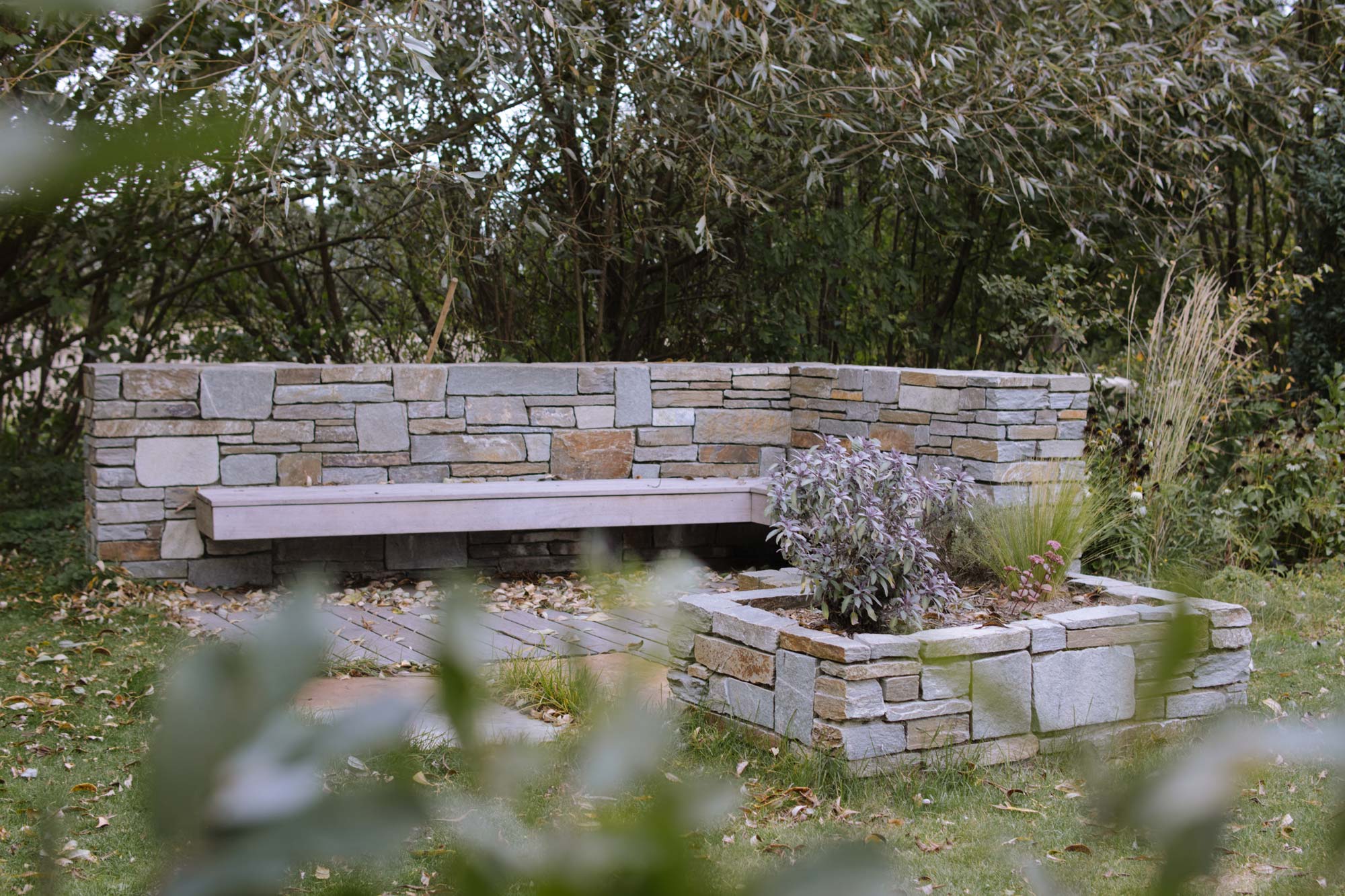 Homann-Landschaften-Garten--und-Landschaftsarchitektur-natursteinmauer-lounge-feuerstelle-hochbeet-stenari-sitzbank-abendsonne